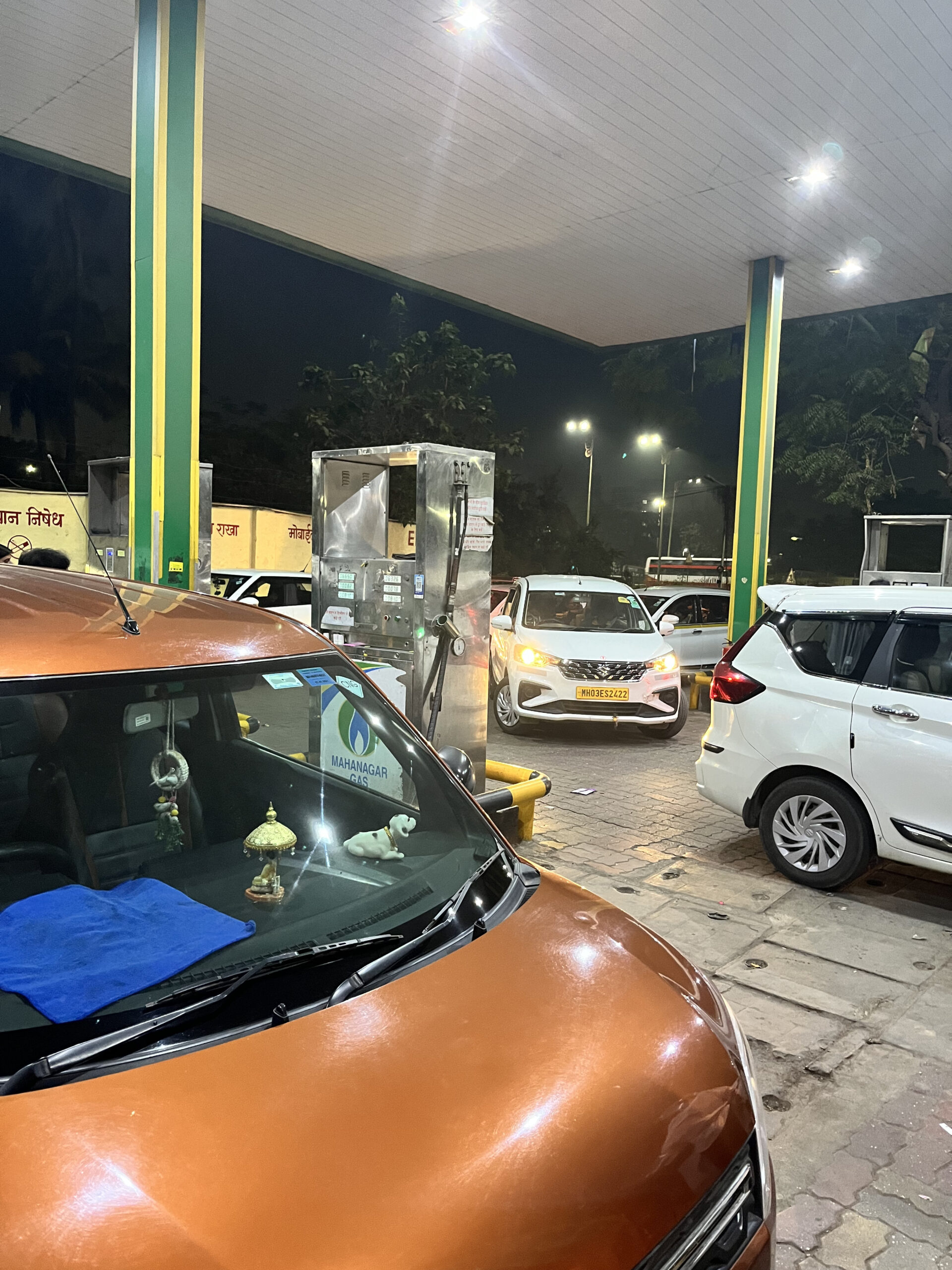 夜のインド地元ガソリンスタンドの給油渋滞シーン。給油機の前に複数の車が斜めから入り込んでいる